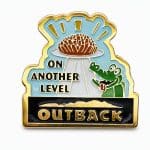lapel pin showing a hungry croc looking up at a hot plate of Bloomin' Onion, with the phrase "On Another Level" and the Outback logo, crafted by The Pin Center