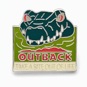 Glow-in-the-dark lapel pin featuring an angry looking croc saying "take a bite out of life" with the Outback logo, created by The Pin Center