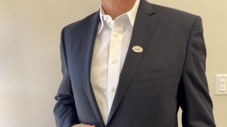 A man in a tailored corporate suit wearing a custom bro brooch on his lapel, highlighting the bold metal finish and modern design of the accessory.